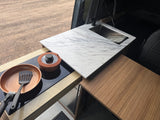 Inside an rv rental: A sleek camper kitchen features a marble countertop, sink, faucet, and induction cooktop with cookware.