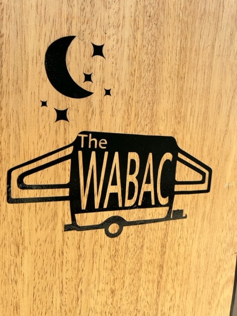 Black 'The WABAC' RV rental logo on wood, shaped like a camper van with moon and stars, hinting at night adventures. — photo 2