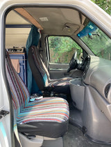 RV rental van interior, showing colorful patterned front seats and a custom bed area behind for travelers.