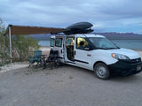 Enjoy an rv rental! This converted van features an awning, chairs, and table, set up for peaceful lakeside camping.