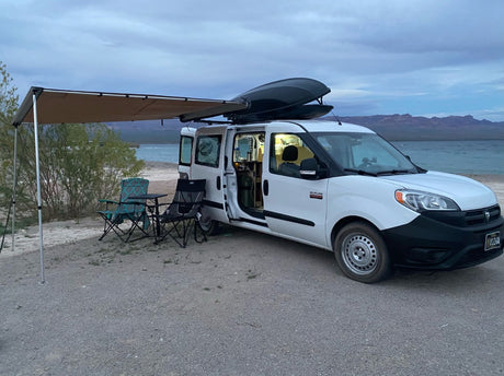 Enjoy an rv rental! This converted van features an awning, chairs, and table, set up for peaceful lakeside camping.
