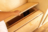 A hand opens a wooden storage compartment, part of the custom interior of an RV rental, revealing hidden space.