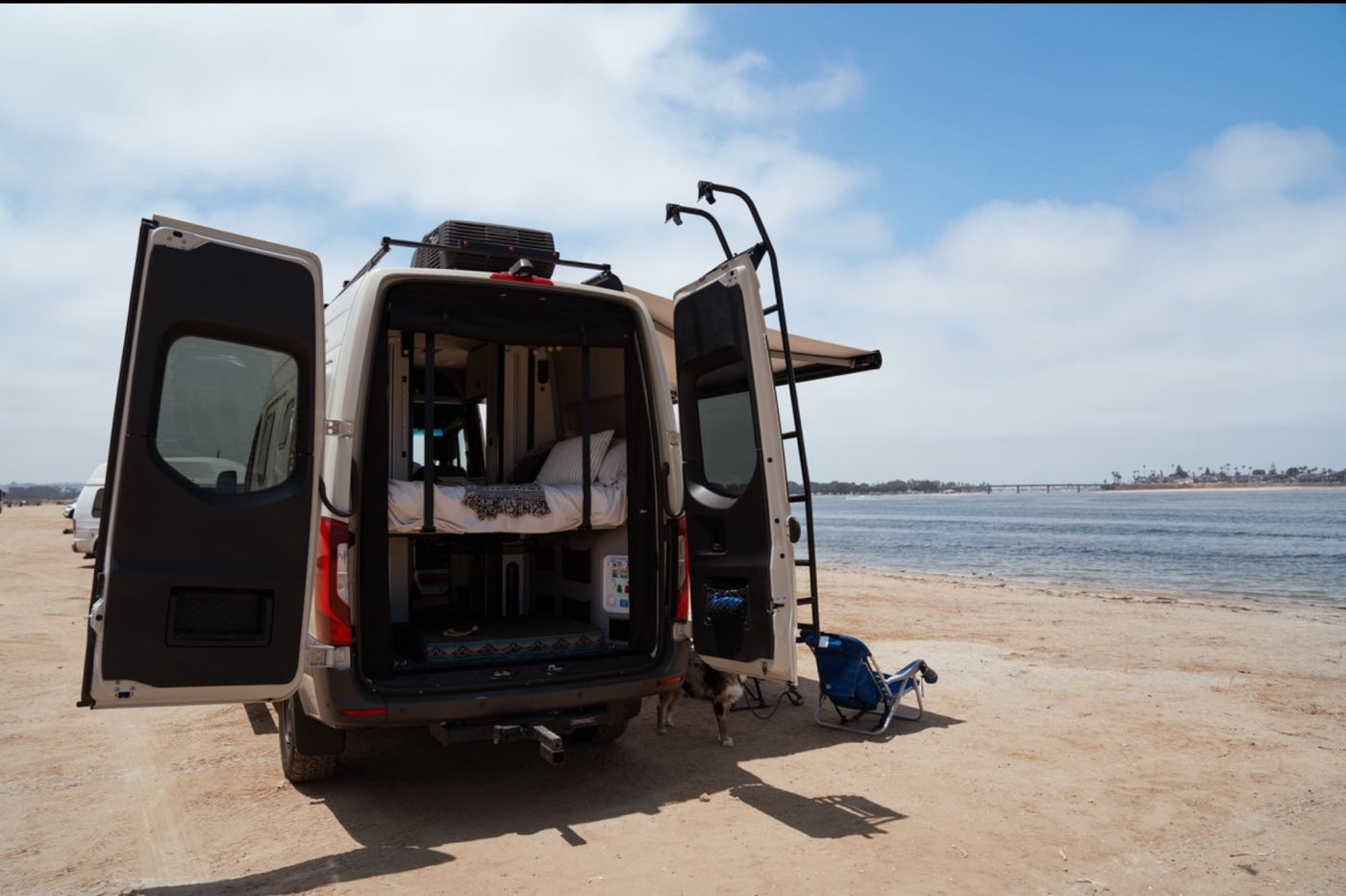  overlooking a serene ocean and sandy shore.|Hands fill a green bowl with water from a sleek faucet in an RV rental's compact kitchen.|Group enjoys an RV rental van adventure in a damp forest. A light-colored Winnebago with an awning out — photo 7