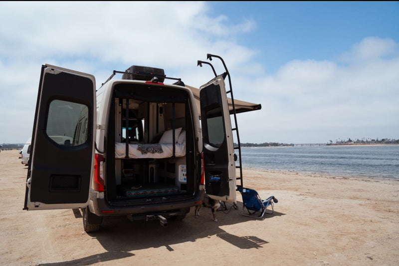  overlooking a serene ocean and sandy shore.|Hands fill a green bowl with water from a sleek faucet in an RV rental's compact kitchen.|Group enjoys an RV rental van adventure in a damp forest. A light-colored Winnebago with an awning out — photo 7