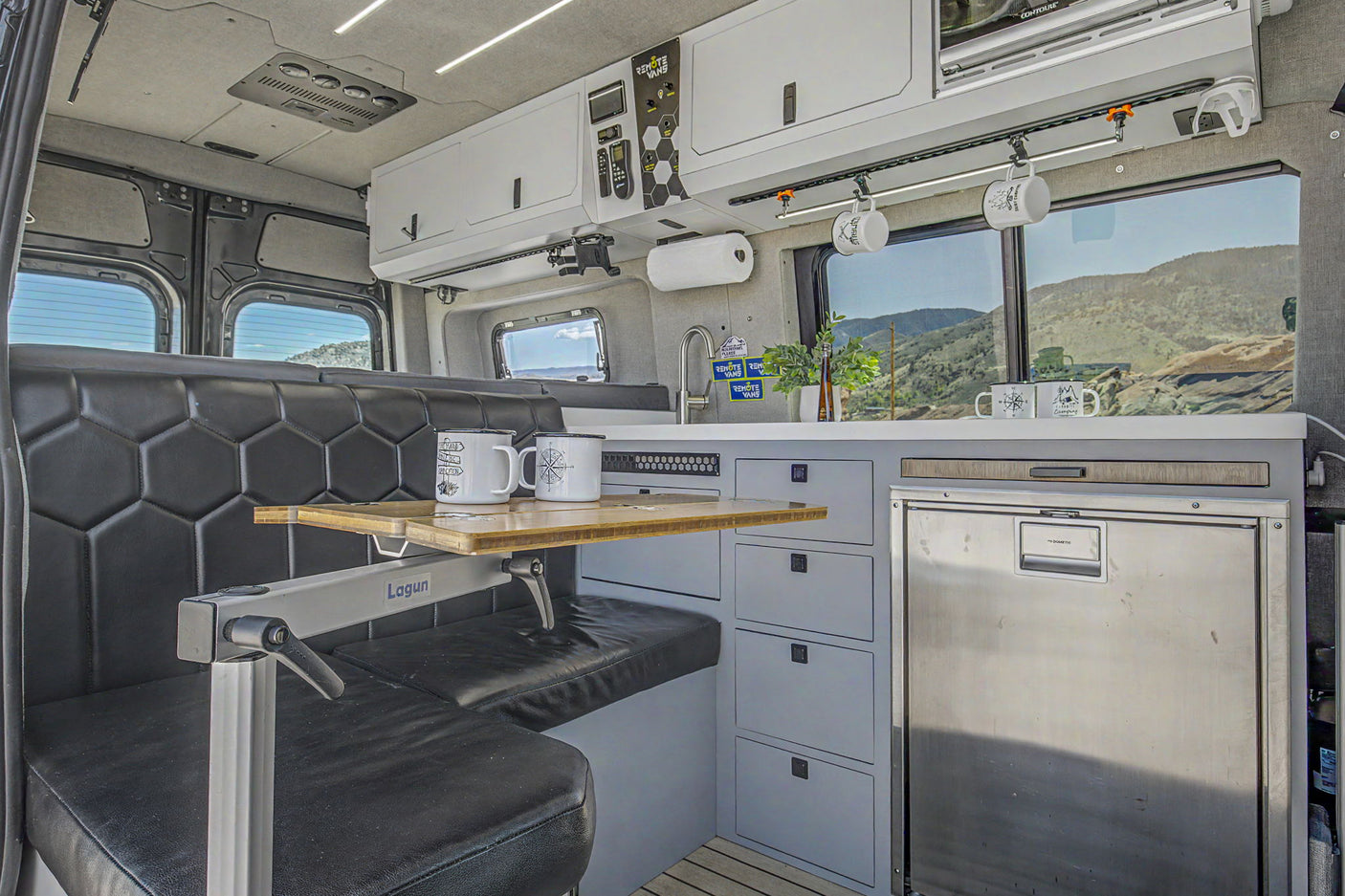 This RV rental camper van interior features a compact kitchen, dining space, and scenic mountain views for adventure.