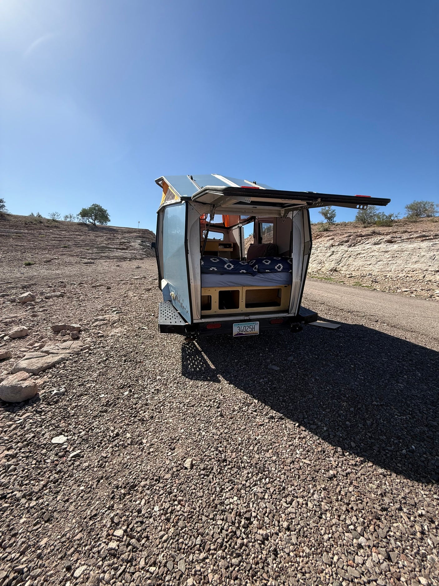 Open rear of an RV rental pop-top camper in a sunny desert. Bed, storage visible for camping travel.