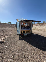 Open rear of an RV rental pop-top camper in a sunny desert. Bed, storage visible for camping travel.