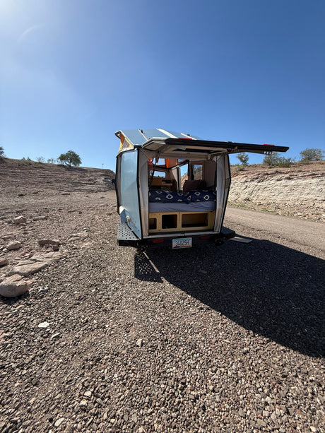 Open rear of an RV rental pop-top camper in a sunny desert. Bed, storage visible for camping travel.