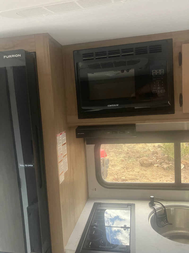 Compact rv rental kitchen: black refrigerator, microwave, gas stovetop, and sink. Efficient galley setup for travel adventures. — photo 12