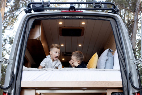 Two kids enjoy an RV rental, playing on the comfy bed in the open back of a camper van. Family adventure awaits!