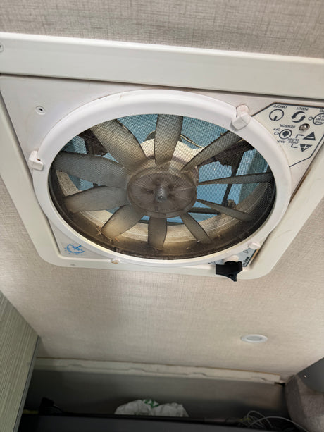 Overhead MaxxAir ceiling fan (dusty) with airflow & rain sensor controls in an RV rental for ventilation.