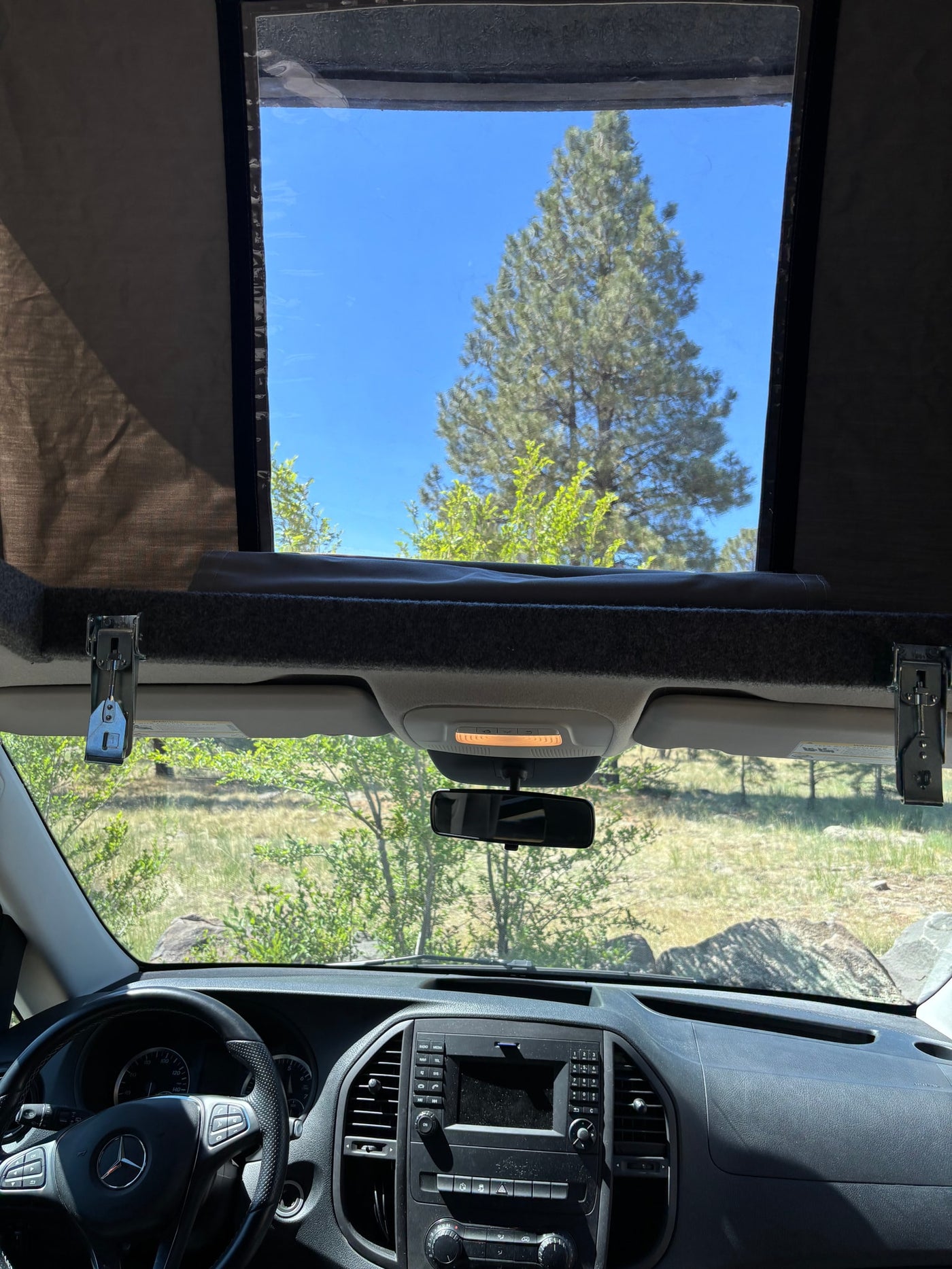RV rental interior view: dashboard, steering wheel, and a pop-top roof open to a pine tree & blue sky. — photo 7