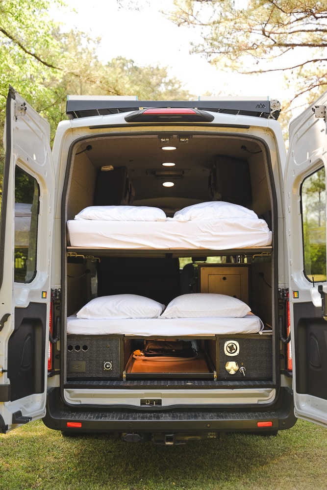  parked on grass. Ideal for your next rv rental adventure.|RV rental van's organized interior features stacked bunk beds and lower storage for travel.|RV rental: Inside a camper van — photo 2