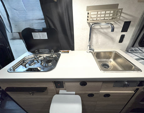 Compact RV rental kitchenette featuring a stove, sink, and counter, with a toilet tucked neatly below.