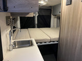 Cozy RV rental interior with kitchenette, bed, and storage. Perfect for adventures.