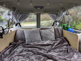 Cozy RV rental bed with string lights & curtains, perfect for comfortable travel inside a customized camper van.