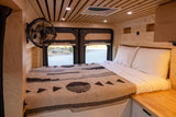 RV rental's inviting wood interior: bed, fan, and ceiling lights, with a view through rear windows.