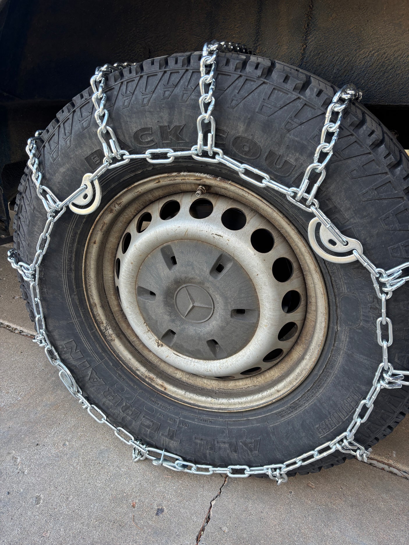 Winter ready RV rental: Close-up of a vehicle tire with new, shiny snow chains installed for maximum winter traction.