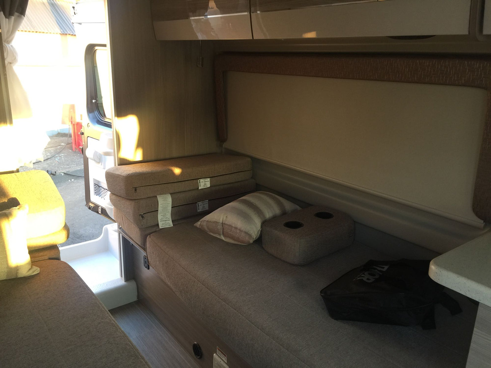 Inside a bright RV rental: compact living space with comfortable bench seating, foldable cushions, and an open side door.