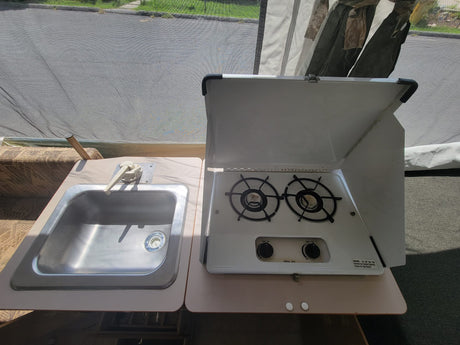 RV rental pop-up camper interior: a compact kitchen with a shiny stainless steel sink and an open two-burner stove.