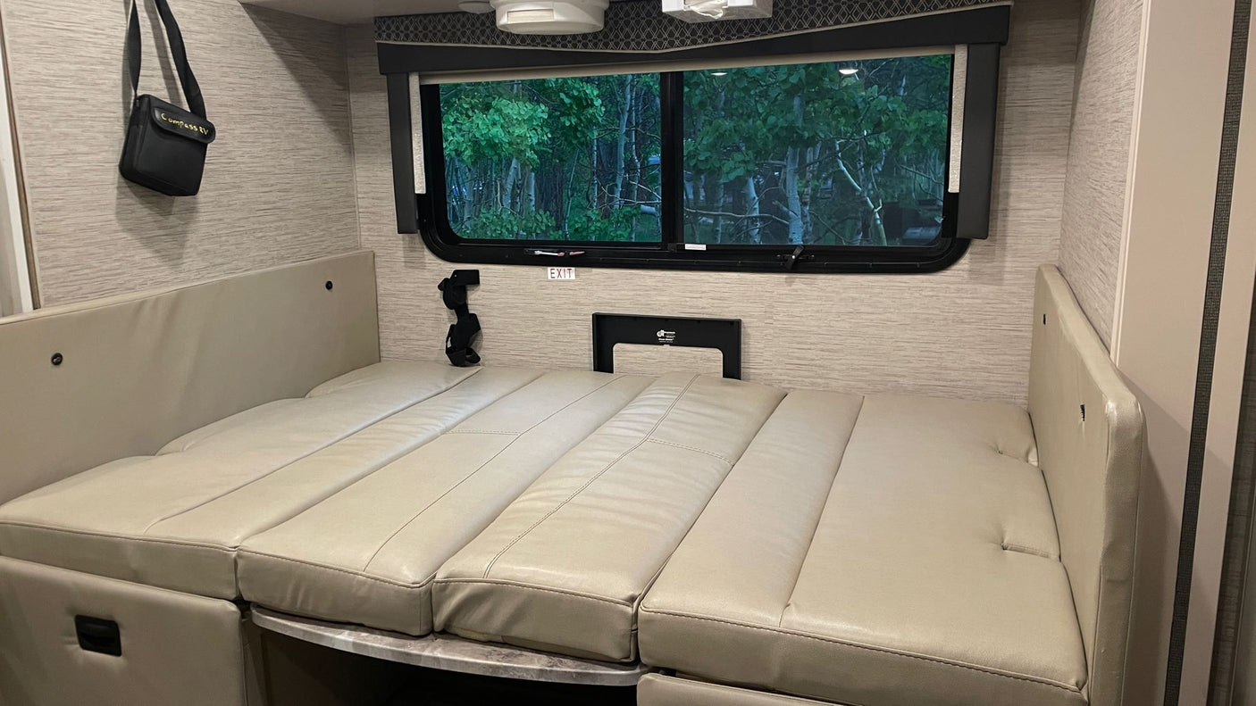 Cozy RV rental interior: Dinette converted to a comfortable sleeping area with a view of the forest outside.