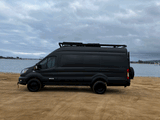 Black Vandoit camper van parked on sandy beach by water. Your next RV rental adventure awaits!