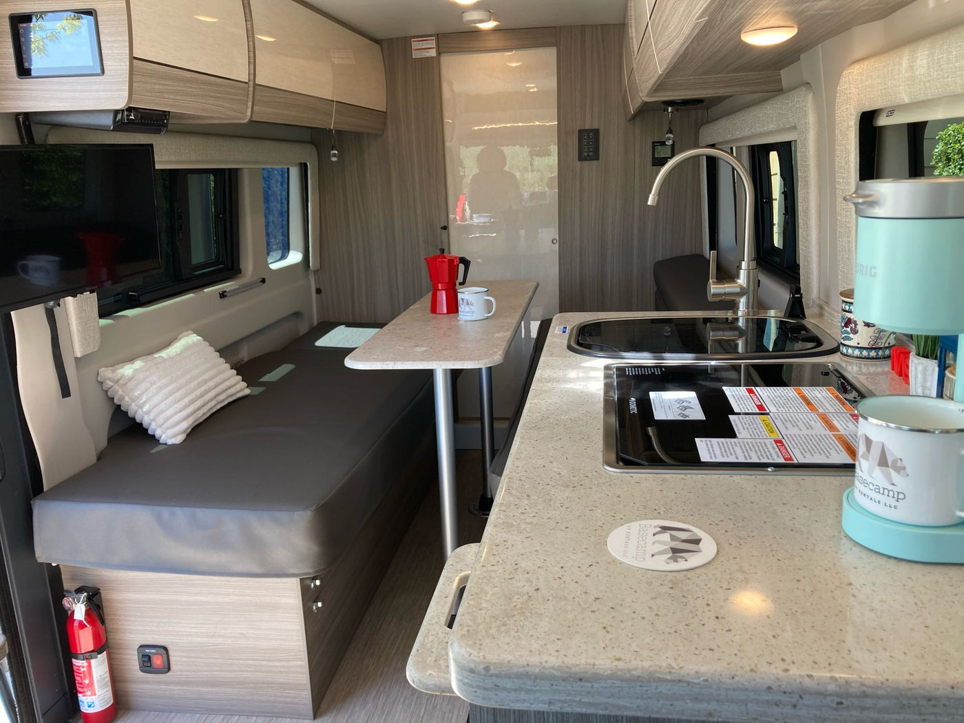 RV rental interior: compact kitchen with sink & stovetop, a coffee station, TV, and bench seating. — photo 11