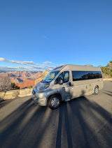 An RV rental offers stunning views of the Grand Canyon's vast red layers under a clear blue sky. Perfect for scenic road trips.