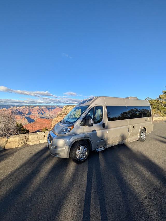 An RV rental offers stunning views of the Grand Canyon's vast red layers under a clear blue sky. Perfect for scenic road trips.