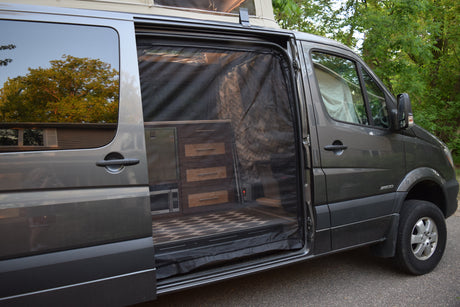 Explore this RV rental's cozy interior: a grey van with its side door open, featuring custom cabinets, microwave, and a bug screen.