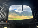 Inside an RV rental rooftop tent, enjoy a scenic mountain view over golden fields and distant hills. Perfect for camping!