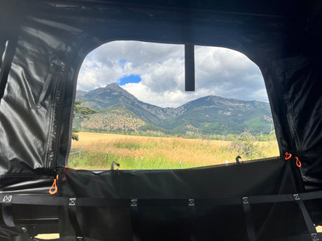 Inside an RV rental rooftop tent, enjoy a scenic mountain view over golden fields and distant hills. Perfect for camping!
