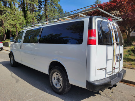 White Chevy Express van with a sturdy roof rack and rear ladder, suitable for an RV rental adventure or conversion.