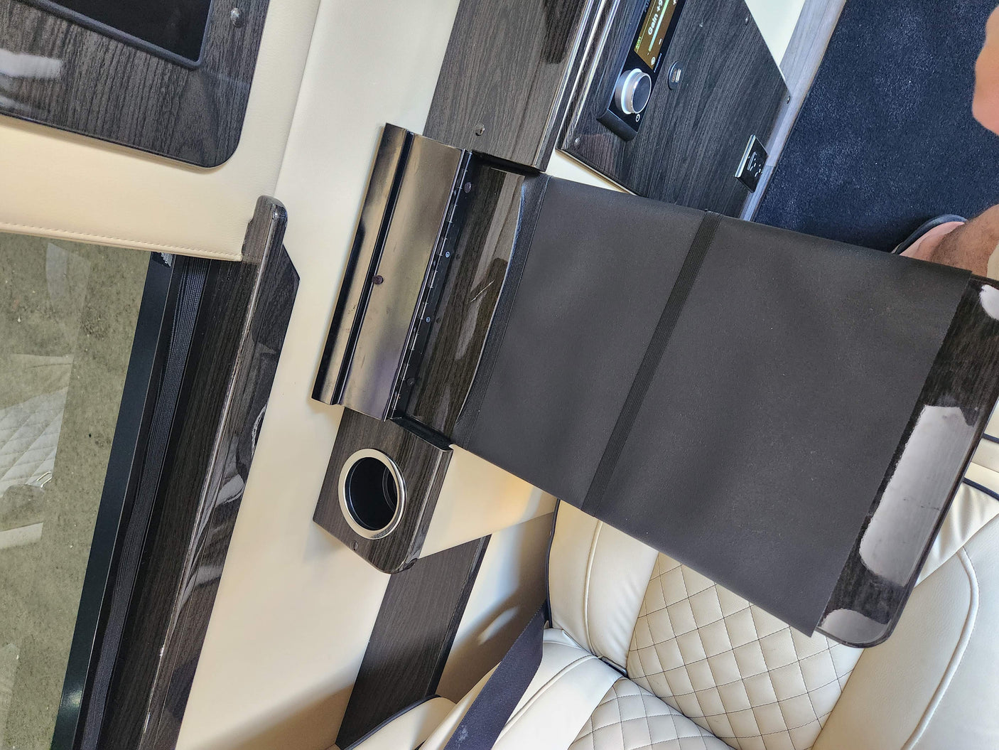 Luxurious RV rental interior with cream leather seats, dark wood accents, and a control panel next to a flat black surface.