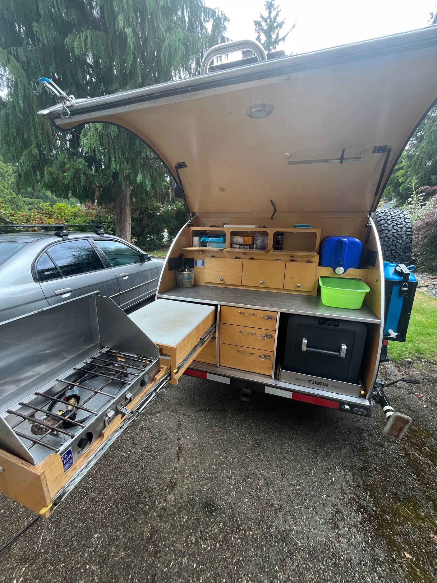 This RV rental's open hatch reveals a compact outdoor kitchen: pull-out stove, fridge, water, & storage. Ideal for camping.