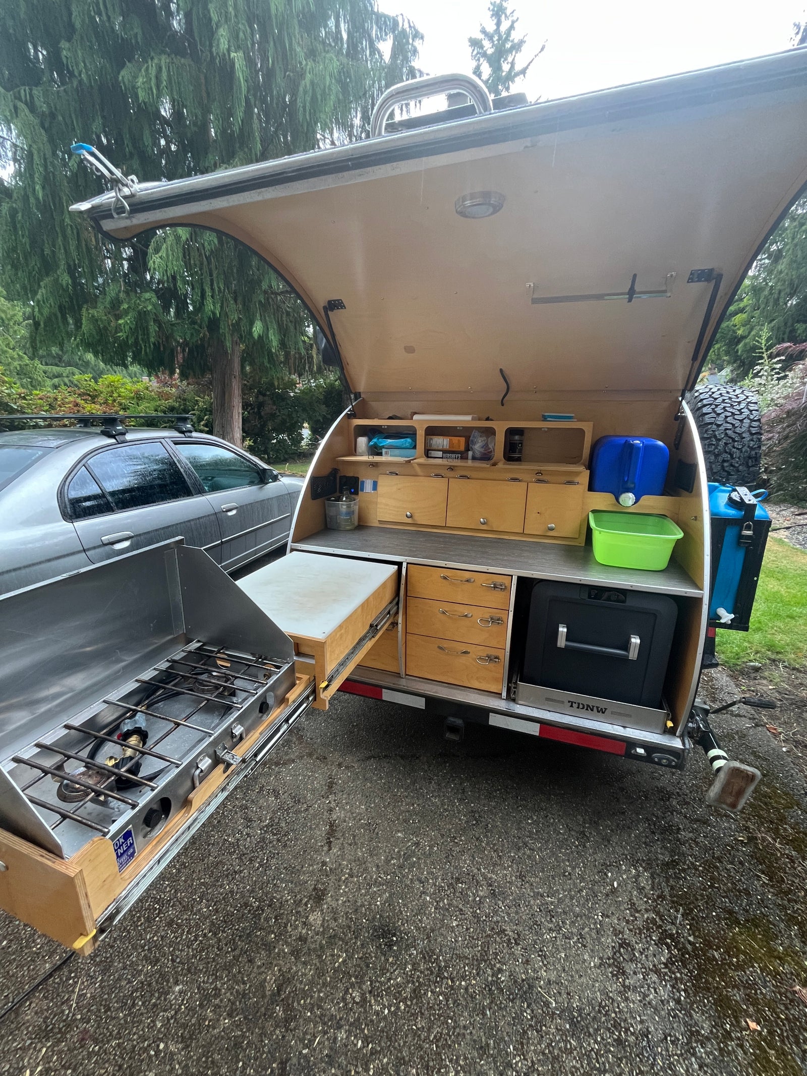 This RV rental's open hatch reveals a compact outdoor kitchen: pull-out stove, fridge, water, & storage. Ideal for camping.