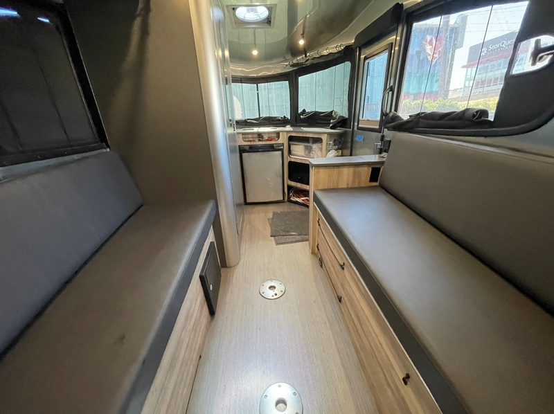 Inside an rv rental, showing two long benches, a kitchen area with a fridge, and large windows revealing an urban view. — photo 7