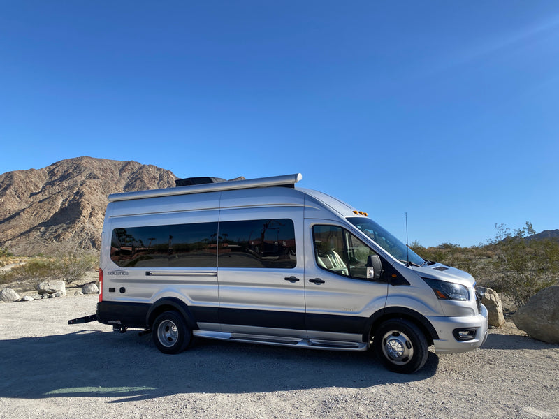 A silver Jayco Solstice RV rental is parked on a gravel path in a sunny desert landscape with rugged mountains. — photo 5