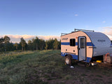 An RV rental, a Sunray Sport camper, parked in a grassy field with trees under a partly cloudy sky during golden hour.