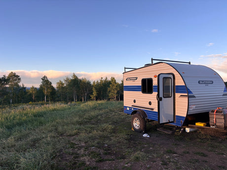 An RV rental, a Sunray Sport camper, parked in a grassy field with trees under a partly cloudy sky during golden hour.