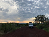 Scenic rv rental experience: white van on a dirt road, admiring a vibrant cloudy sunset over distant mountains.