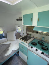 Inside this retro rv rental: a stylish light blue kitchenette, complete with a stove and sink, and a comfortable bed.