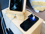 An RV rental interior: a smartphone on a bamboo stand charges via a blue-lit 12V USB port on a light wood surface.