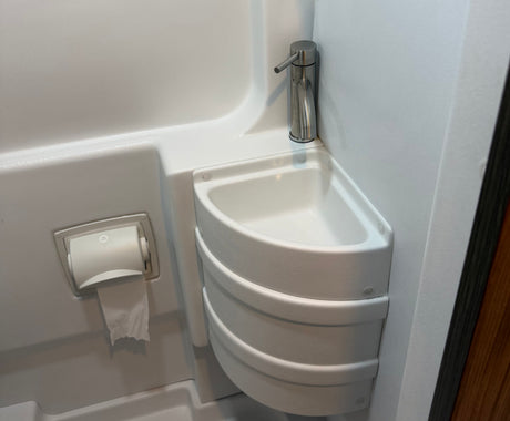 Compact RV rental bathroom featuring a corner sink, sleek faucet, and mounted toilet paper holder in a small, functional space.