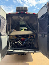 RV rental's rear entry showing a bed above, two electric bikes below, and a protective mesh screen.