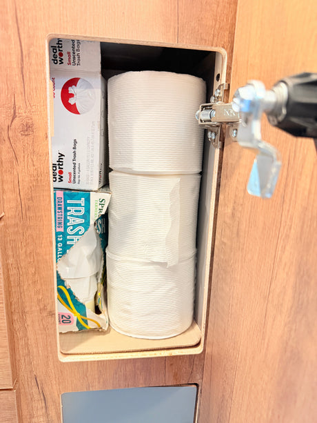 RV rental cabinet stocked with toilet paper and various trash bags, indicating organized travel essentials for guests.