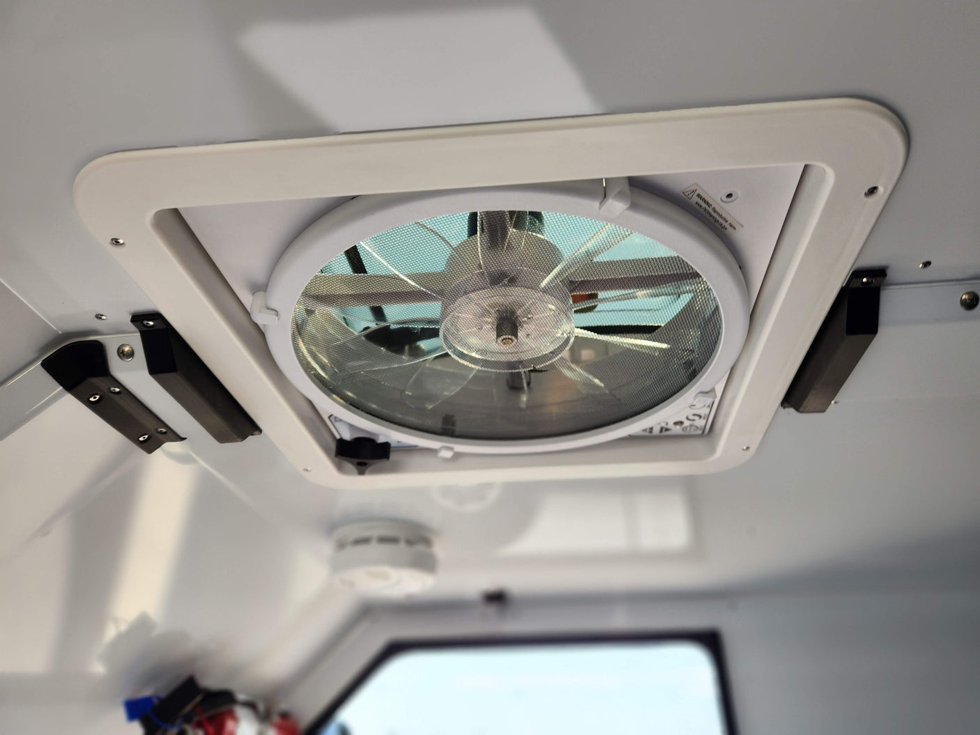 An RV rental's ceiling featuring a white vent fan with a mesh screen and a smoke detector for comfort and safety.