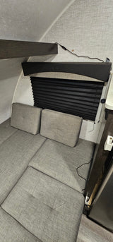 RV rental interior: View of convertible gray seating/bed, black window blind, and wall texture in a compact camper.