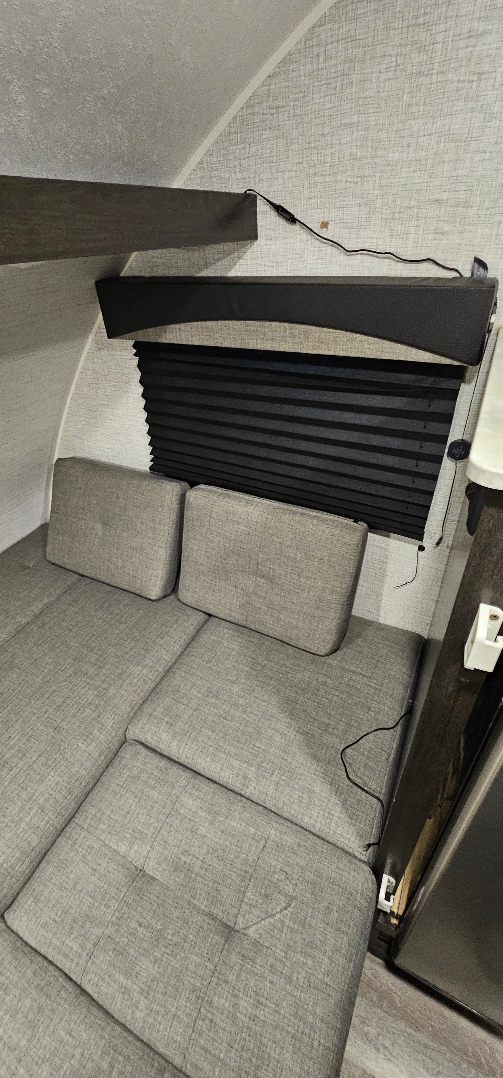 RV rental interior: View of convertible gray seating/bed, black window blind, and wall texture in a compact camper.