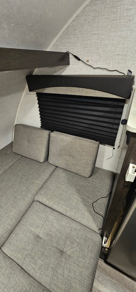 RV rental interior: View of convertible gray seating/bed, black window blind, and wall texture in a compact camper.